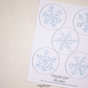 Pu&ograve; includere: Banner circolare di fiocchi di neve stampabile. Cinque disegni di fiocchi di neve blu ad acquerello su sfondo bianco. Il testo "Pretty Plain Paper Circle Banner" e le istruzioni per stampare, tagliare e fissare a una corda o un nastro con nastro adesivo o colla sono inclusi.