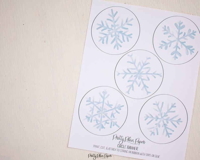 Pu&ograve; includere: Banner circolare di fiocchi di neve stampabile. Cinque disegni di fiocchi di neve blu ad acquerello su sfondo bianco. Il testo "Pretty Plain Paper Circle Banner" e le istruzioni per stampare, tagliare e fissare a una corda o un nastro con nastro adesivo o colla sono inclusi.