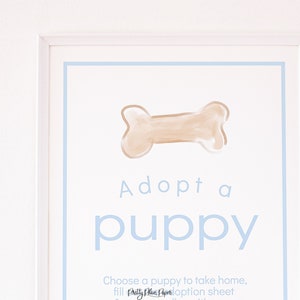 May include: A white framed sign with a blue border and the text "Adopt a puppy" in blue lettering. A brown bone is drawn at the top of the sign.