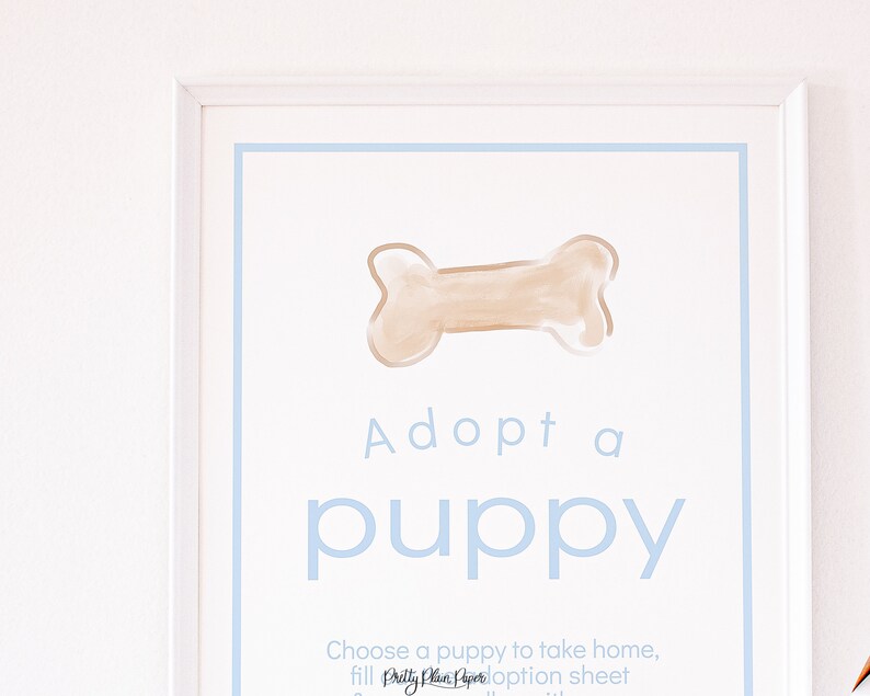 May include: A white framed sign with a blue border and the text "Adopt a puppy" in blue lettering. A brown bone is drawn at the top of the sign.