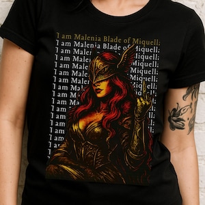 May include: Black t-shirt with a graphic of a warrior with red hair and a golden helmet, and the text "I am Malenia Blade of Miquella." The shirt is worn by a person with dark hair and dark lipstick.