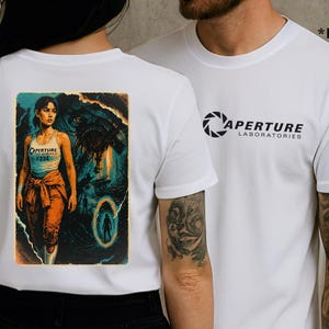 May include: White t-shirts with graphic designs. One shirt features the Aperture Laboratories logo in black. The other shirt displays a colorful image of a woman in an orange jumpsuit, with the text "Aperture #234".