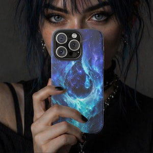 May include: A smartphone case featuring a vibrant nebula design in shades of blue and teal. The case has a glossy finish and a camera cutout. The phone case is held up in front of a person's face.
