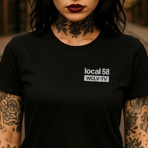 Peut inclure: T-shirt noir à col rond avec le texte "local 58" et "WCLV-TV" dans un rectangle blanc sur la poitrine. Le t-shirt est fait d'une matière douce. L'image montre le haut du corps d'une personne.