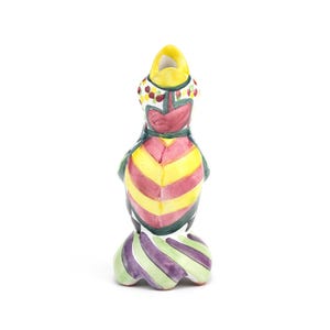 May include: A colorful ceramic bird figurine with a yellow head and a body featuring yellow and red stripes. The bird has a green and purple striped base and is decorated with red, white, and green accents.