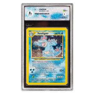 Può includere: Una carta Pokémon valutata con Feraligatr, una creatura blu simile a un coccodrillo. La carta è del set Neo Genesis, valutata 8.5 NM-MT+. La carta ha testo in italiano e inglese, con un design olografico e 120 PV.