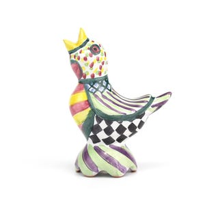 May include: A colorful ceramic bird figurine with a yellow crown and a patterned body. The bird features a mix of stripes, checks, and polka dots in various colors, including red, green, yellow, and purple. The figurine has a whimsical and artistic design.