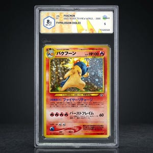Könnte beinhalten: Eine bewertete Pokémon-Karte mit Typhlosion (Holo) aus der Serie Gold, Silver, to a New World. Die Karte ist in einem Schutzhalter eingeschlossen und hat eine Bewertung von 8,5. Das Kartenkunstwerk zeigt eine gelbe und blaue Kreatur mit japanischem Text.
