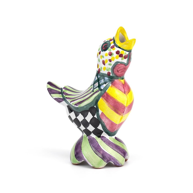 May include: A colorful ceramic bird figurine with a yellow beak and a patterned design. The bird features a mix of colors, including yellow, red, green, and black, with stripes, polka dots, and checkered patterns. The figurine has a rounded base.