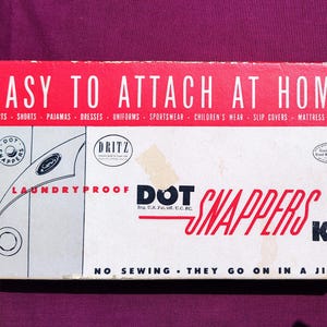 May include: A white box with red lettering that reads "Easy to Attach at Home" and "Dot Snappers Kit". The box features a laundry-proof design and instructions for attaching the snaps. The box is for a kit of laundry-proof snaps.