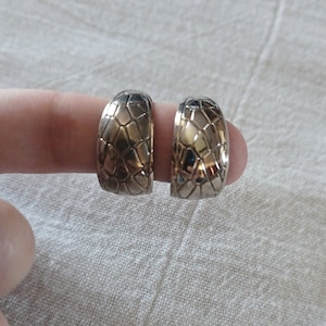 May include: A pair of silver hoop earrings with a textured geometric design.