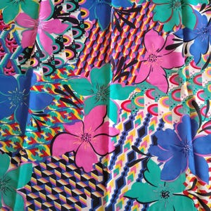 May include: A colourful floral fabric with large flowers in pink, blue, and teal. The design is set against a patchwork of geometric and abstract patterns. The fabric has a white background with a pink border.