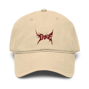 Peut inclure: Casquette de baseball beige avec une visière incurvée. Le chapeau présente un motif graphique stylisé rouge foncé sur le devant. Il a un bouton sur le dessus et une sangle réglable à l'arrière.