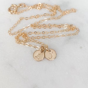 May include: A gold chain necklace with two small gold charms, each with a letter engraved on it. The letters are "I" and "J".