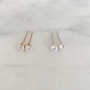 May include: Two pairs of stud earrings, one pair is gold and the other is silver. Both pairs feature a clear round stone.