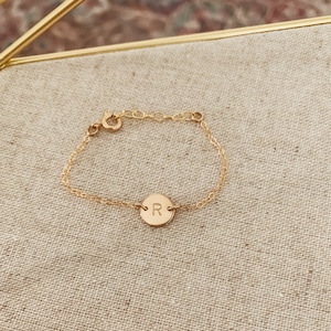Peut inclure: Un bracelet en chaîne dorée avec un petit charme rond gravé de la lettre "R".