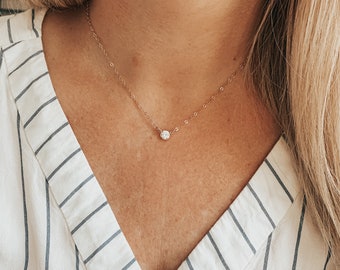 May include: A delicate gold chain necklace with a small, clear, round gemstone pendant.