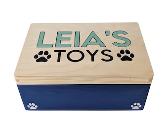 Peut inclure: Une boîte de rangement rectangulaire en bois avec un couvercle en bois clair naturel et une base bleu foncé. Le couvercle porte l'inscription LEIA'S TOYS en lettres vert clair et noires, entourée de deux empreintes de pattes noires.