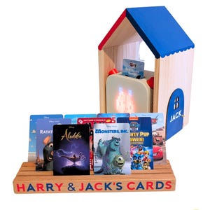 May include: A wooden house-shaped media player with a blue roof and a door labelled JACK, accompanied by a wooden card holder base with the text HARRY & JACK'S CARDS. Several rectangular cards featuring Disney and Nickelodeon characters are displayed.