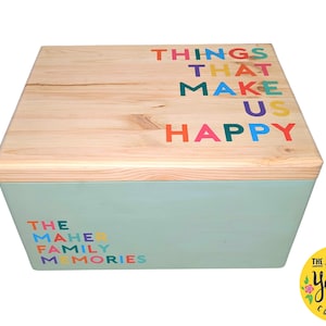 May include: A wooden storage box with a light blue base and a natural wood lid. The lid features the words "THINGS THAT MAKE US HAPPY" in colourful letters. The box also has the words "THE MAHER FAMILY MEMORIES" on the side.