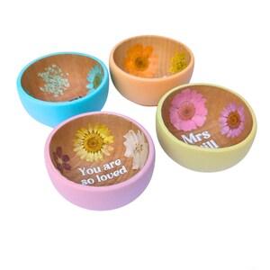 May include: Four small wooden bowls with colourful exteriors and dried flower accents. The bowls are painted in light blue, peach, pink, and yellow. One bowl has the text "You are so loved" and another has the text "Mrs. Jill".