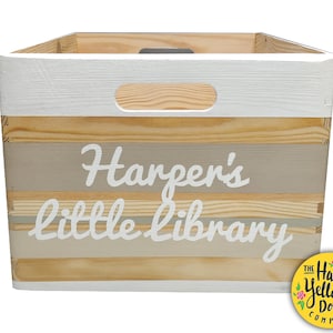 May include: A rectangular wooden storage crate with a white painted top rim and handle cutouts. The front features horizontal stripes in natural wood, beige, and gray tones with the white text Harper's little library printed across the center.