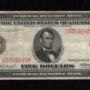 Peut inclure: Un billet de cinq dollars de la Réserve fédérale vintage. Le billet présente un portrait d'Abraham Lincoln et le texte "FIVE DOLLARS". Le numéro de série D3306545A est imprimé en rouge. Le billet est encadré de volutes ornées et du texte "THE UNITED STATES OF AMERICA."