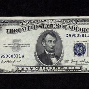 May include: A vintage five-dollar bill from The United States of America. The bill features a portrait of Abraham Lincoln and the text "FIVE DOLLARS IN SILVER PAYABLE TO THE BEARER ON DEMAND". The bill is primarily green and black.
