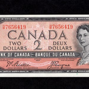 Pode incluir: Uma nota de dois dólares canadenses vintage. A nota apresenta a palavra "CANADA" em letras grandes, juntamente com a denominação "TWO DOLLARS" e "DEUX DOLLARS". Um retrato de uma mulher está à direita. A nota tem um esquema de cores rosa e preto.