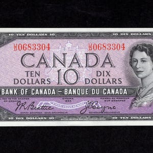 以下が含まれることがあります： カナダのヴィンテージ10ドル紙幣。紙幣には、右側に女性の肖像画と中央に「CANADA TEN DOLLARS DIX DOLLARS」の文字が描かれています。シリアル番号は赤色で表示されています。