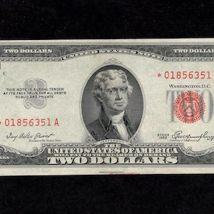 May include: A two-dollar bill featuring a portrait of Thomas Jefferson. The bill has the text "TWO DOLLARS" and "UNITED STATES OF AMERICA". The serial number is 01856351 A.