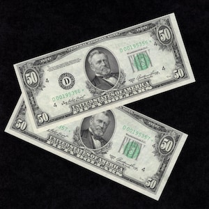 May include: Two fifty-dollar bills on a black background. Each bill features a portrait of Ulysses S. Grant, the text "UNITED STATES OF AMERICA", and the number "50" in multiple locations.