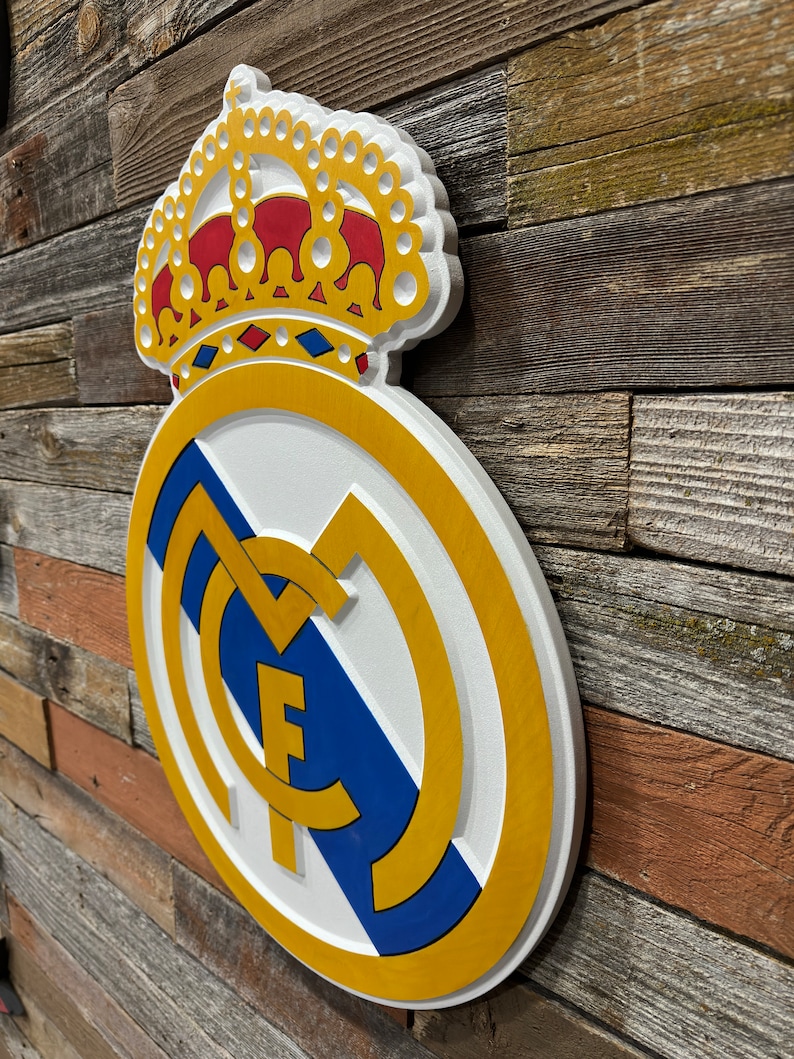 Pode incluir: Um sinal de madeira 3D branco, dourado e azul com o bras&atilde;o do Real Madrid. O bras&atilde;o apresenta uma coroa, uma bola de futebol e as letras "M" e "F".