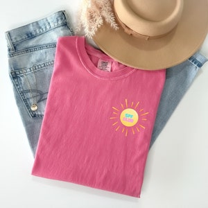 May include: Pink t-shirt with a yellow sun graphic and the text "SPF Club" in pink, blue, and yellow letters.
