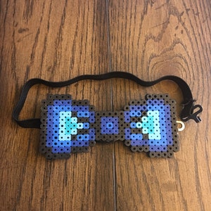 May include: A blue and black pixelated bow tie with an adjustable black elastic band.
