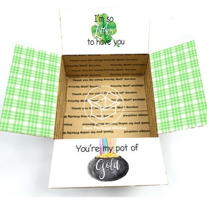 May include: A green and white checkered box with a sticker that says "I'm so lucky to have you" and a pot of gold with a rainbow coming out of it. The sticker also says "You're my pot of gold".
