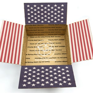 Puede incluir: Una caja de cartón abierta con un diseño de bandera estadounidense roja, blanca y azul. La caja está etiquetada con "Priority Mail Service" y "Care Package Sticker".