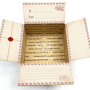 May include: An open cardboard box with a vintage mail service design. The box is lined with brown paper and has a red wax seal on the front. The box is labeled "Priority Mail Service" and "Care Package Sticker". The box is open and ready to be filled with gifts.