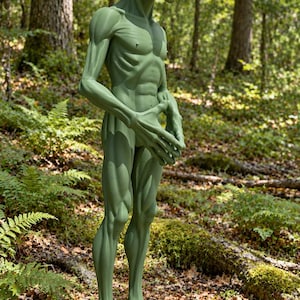 May include: A standing green alien figurine with a large, smooth, oval-shaped head, prominent black almond-shaped eyes, and a slender, muscular humanoid body. The figure has long, thin arms with elongated fingers and defined leg muscles.