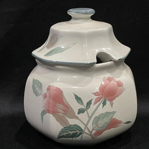 May include: White ceramic sugar bowl with a lid and floral design. The bowl has a green and pink floral pattern with a green trim around the top. The lid has a small spout for pouring.
