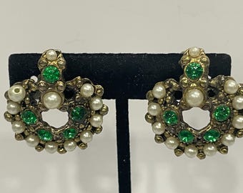 May include: A pair of gold tone earrings with a delicate design featuring green and white stones. The earrings are shaped like a crescent moon and have a vintage look.