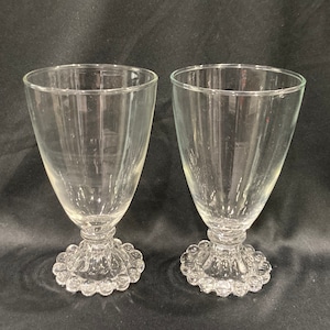 May include: Two clear glass goblets with a textured, beaded base. The goblets are tall and slender with a wide bowl.