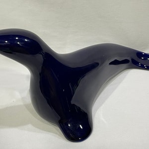 May include: A dark blue ceramic seal figurine. The seal is lying on its belly with its head turned to the side. The figurine is glossy and has a smooth finish.