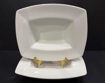 May include: A set of two white rectangular ceramic bowls with wide, flat rims and deep, angled centers. The bowls are stacked, with the top bowl resting on a gold-toned metal display stand that features two curved prongs for support.