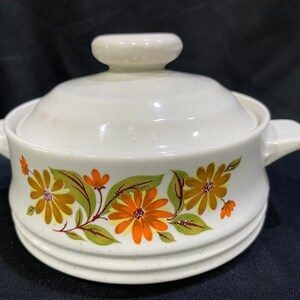 May include: White ceramic casserole dish with a lid. The dish has a floral design with orange, brown, and green flowers.