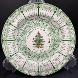 May include: A decorative plate with a green and white design, featuring a calendar for the year 2000. The plate has a Christmas tree in the center and the words "To Celebrate the Millennium".
