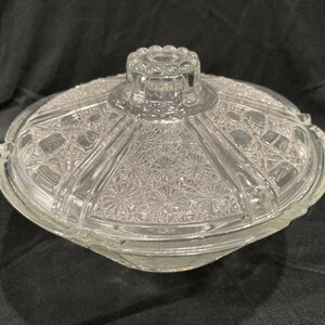 May include: A clear glass covered dish with a decorative pattern. The dish has a domed lid with a knob on top.