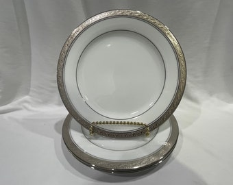May include: Three white ceramic dinner plates with a silver and gold rim. The plates are stacked on top of each other.
