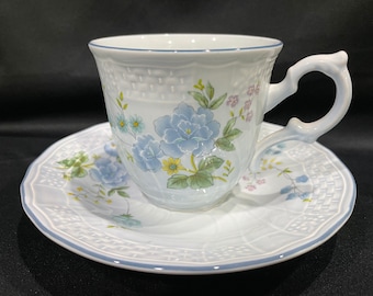 May include: A white teacup and saucer set with a blue and white floral pattern. The cup has a handle and the saucer has a scalloped edge.