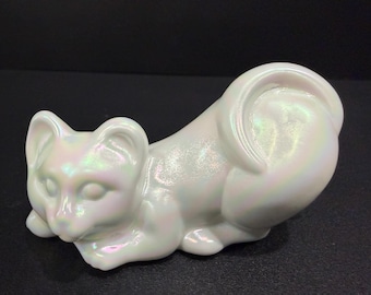 Peut inclure: Une figurine de chat blanc nacré en position de repos. Le chat en céramique a une finition lisse et irisée qui reflète un arc-en-ciel de couleurs. La queue du chat est enroulée et ses yeux sont fermés.